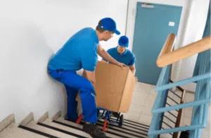 due traslocatori che trasportano su un carrello uno scatolone pesante per delle scale condominiali interne
