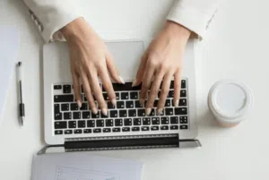 Primo piano sulle mani di una ragazza mentre scrive sul suo computer su una scrivania bianca